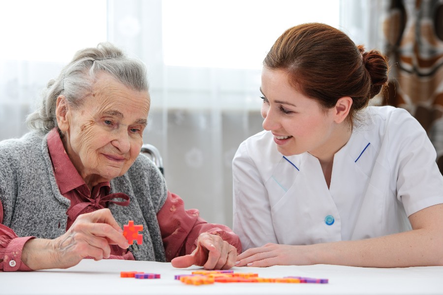 Elder care nurse playing jigsaw puzzle with senior woman in nursing home