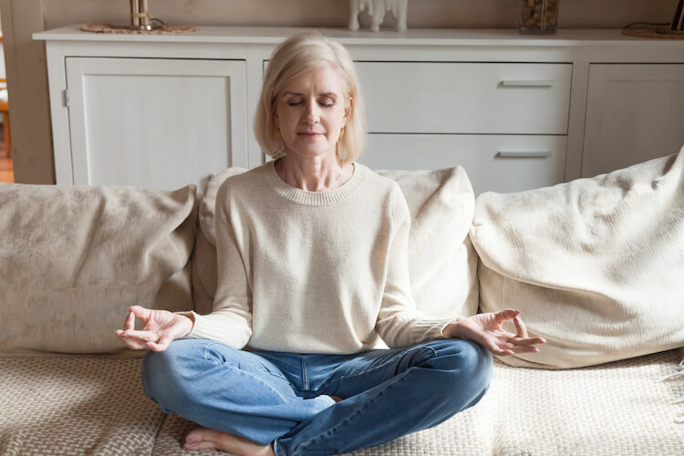 Calm senior woman practicingmeditation on the couch.