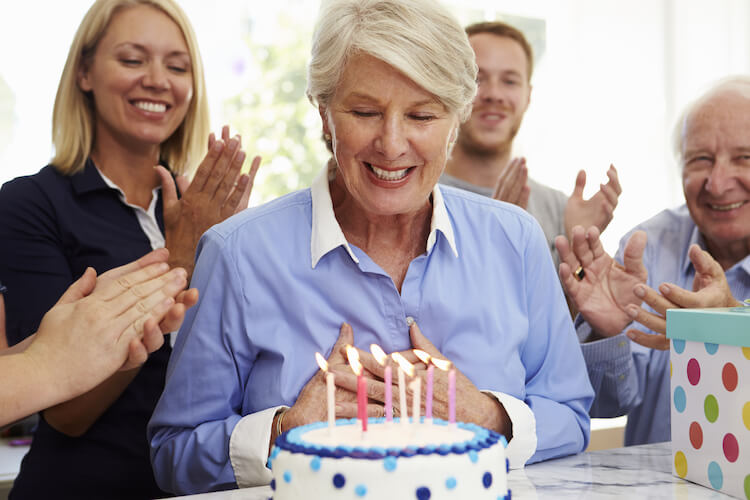 Senior woman blowing out candles on a birthday cake at a family party.