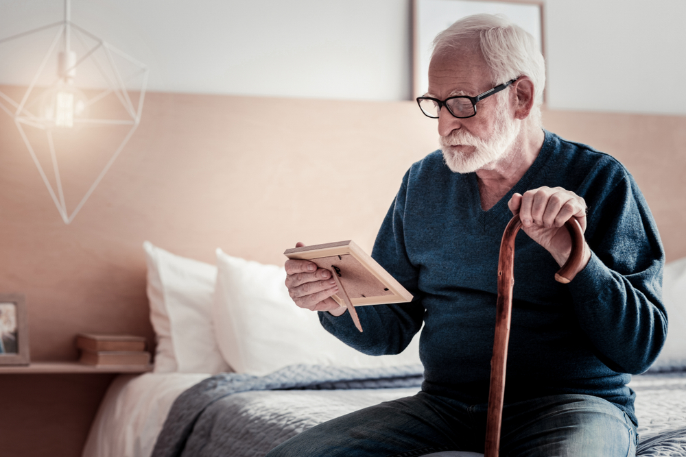 A senior man gets out of bed and looks at a framed photo