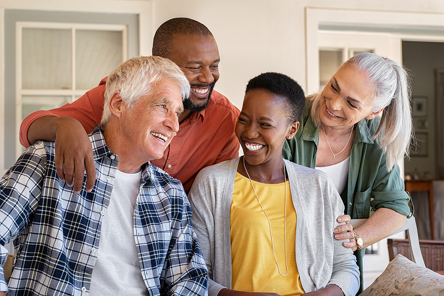 Cheerful friends sitting in courtyard enjoying afternoon together. Group of four mature people sitting outside home and laughing. Happy senior man and old woman enjoying with mature african couple.