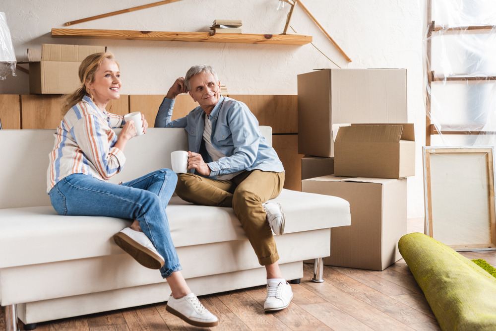 A senior couple take a break on the couch while downsizing and packing things into boxes