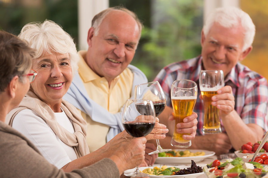 Two older couples smile while toasting with beer and wine