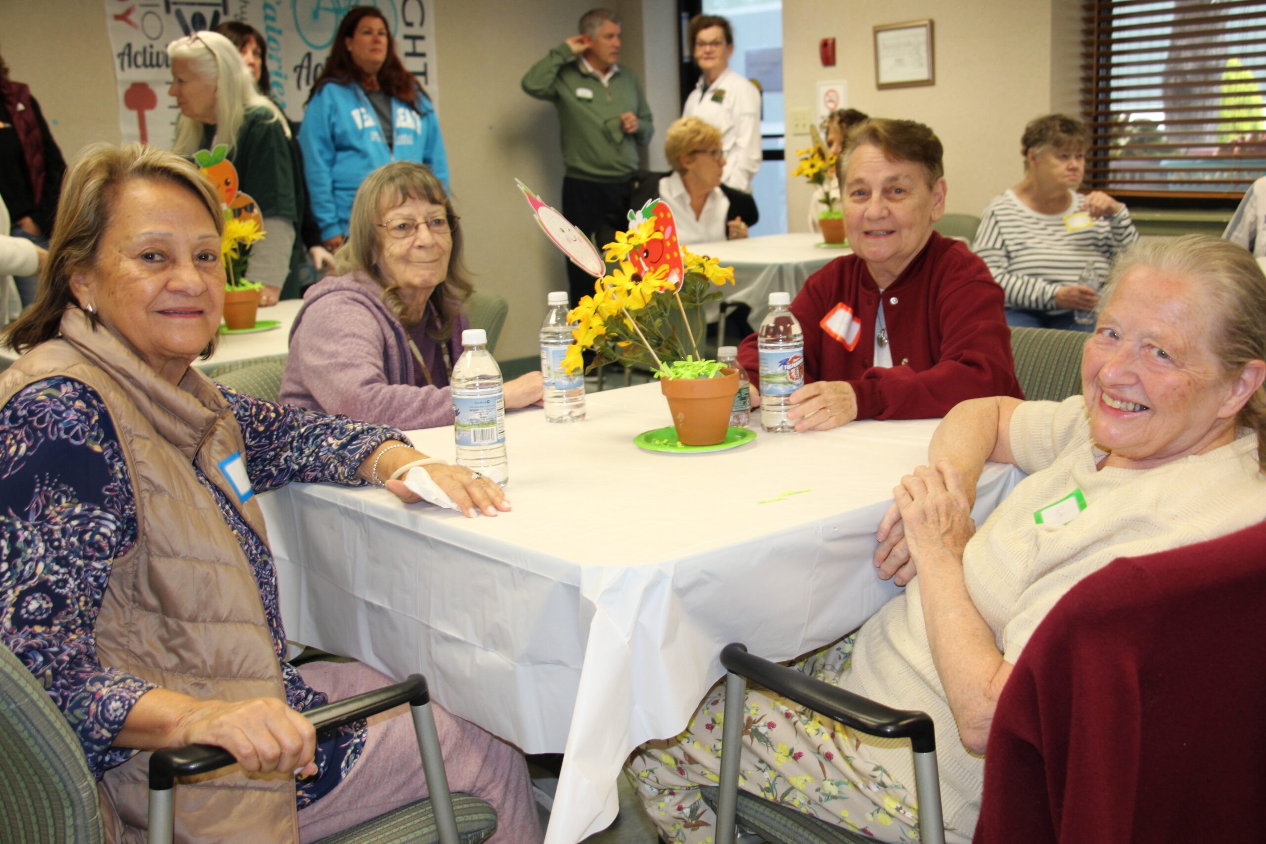 A group of seniors sitting around a table indoors, smiling and posing for a photo.