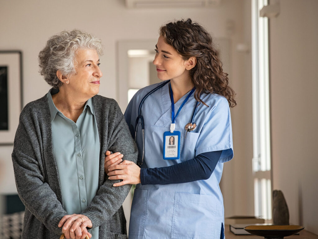 Young caregiver helping senior woman walking. Nurse assisting her old woman patient at nursing home. Senior woman with walking stick being helped by nurse at home.