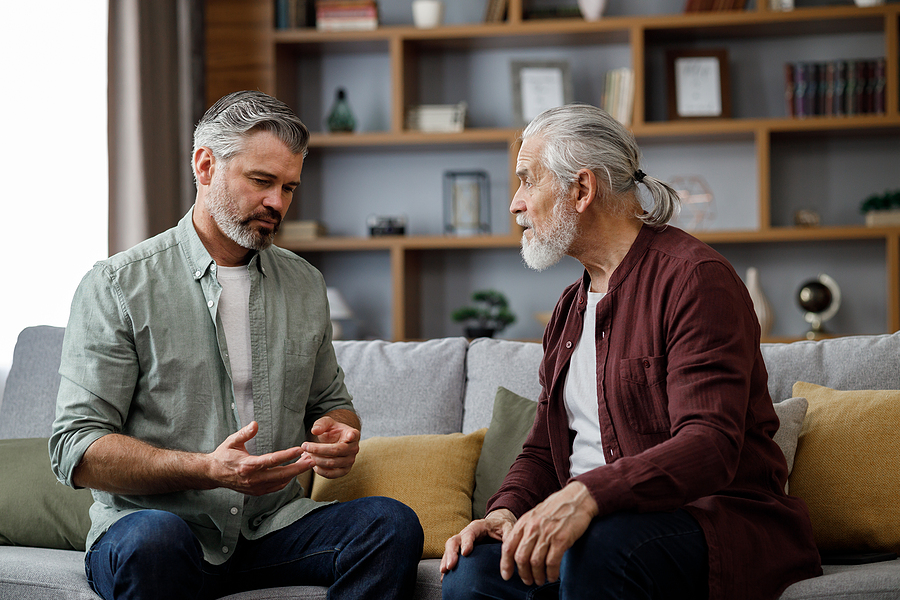 Senior Living Transition Adult son talking to senior father, sitting on a couch.