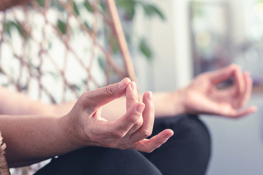 A senior woman is practicing yoga outside, and her hands are in a yoga position.