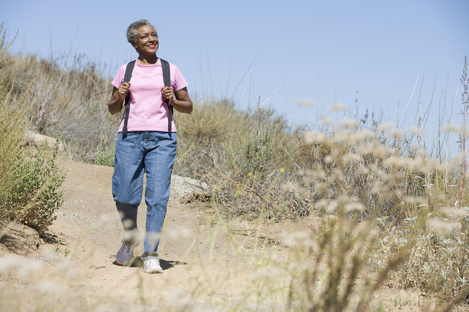 A senior woman walks on a hiking trail with a backpack