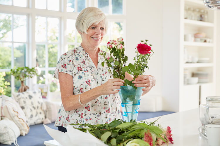 A senior woman arranging flowers in a vase on her kitchen counter.